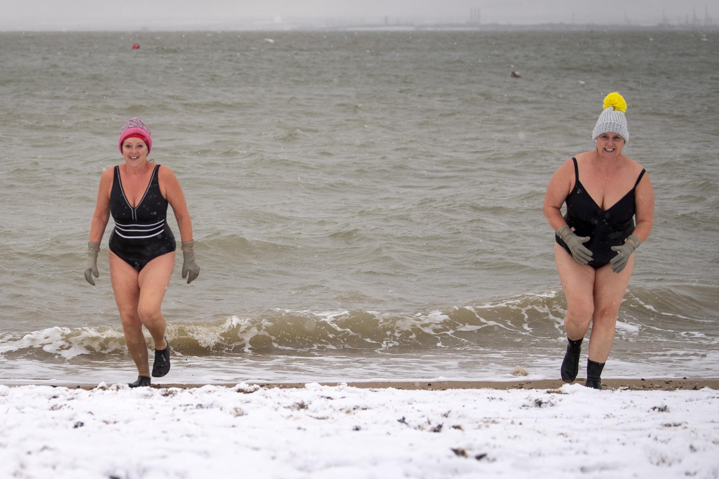 Early morning swimmers Sallyann Manthorp (left) and Peta Hunter walk across snow on the beach after swimming in the 1.4 degree water at Thorpe Bay, Essex, as bitterly cold winds continue to grip much of the nation. Picture date: Tuesday February 9, 2021..