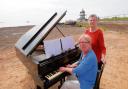 Amazing – Diana Burrell plays the piano at on the beach with artist Annea Lockwood looking on