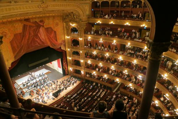 Gazette: A grand theatre with people watching an orchestra. Credit: Canva